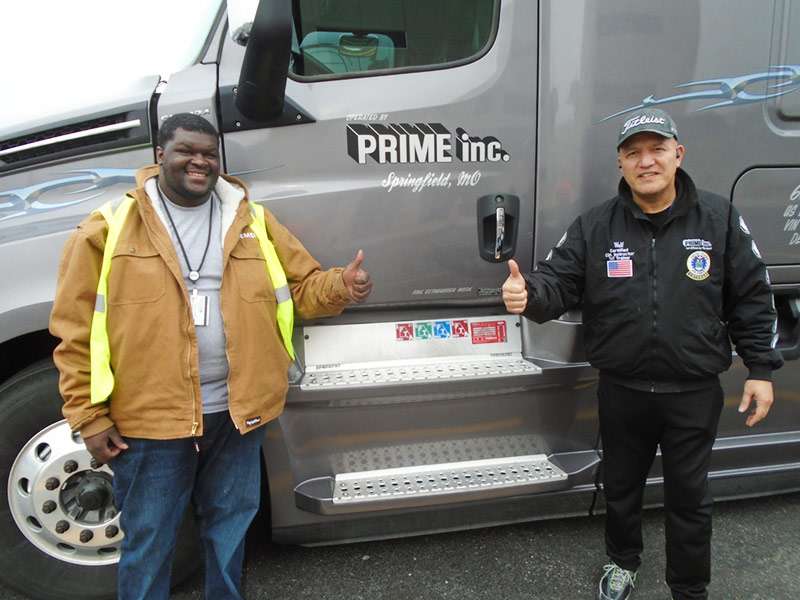 Two male drivers smiling with thumbs up standing in front of a grey Prime truck
