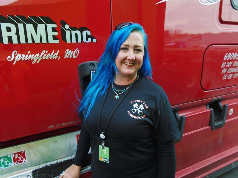 Female driver smiling in front of a red Prime truck