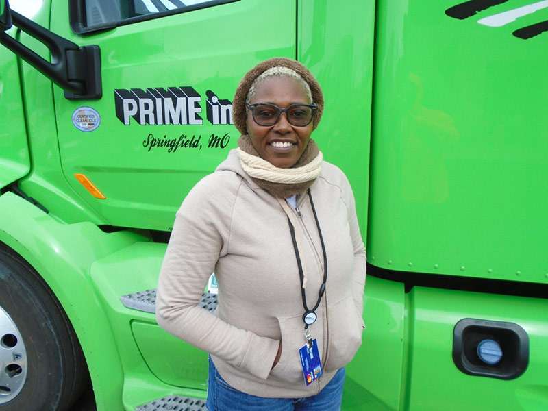 Female driver smiling in front of a green Prime Truck