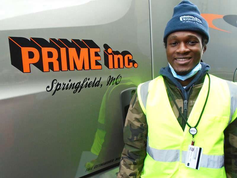 Male driver smiling in front of grey Prime truck